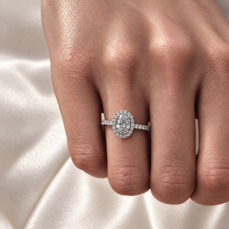 Bague de fiançailles en or blanc 18k sertie d'un diamant éthique de taille ovale avec halo et anneau pavé portée sur une main par la maison de joaillerie Loyal.e Paris